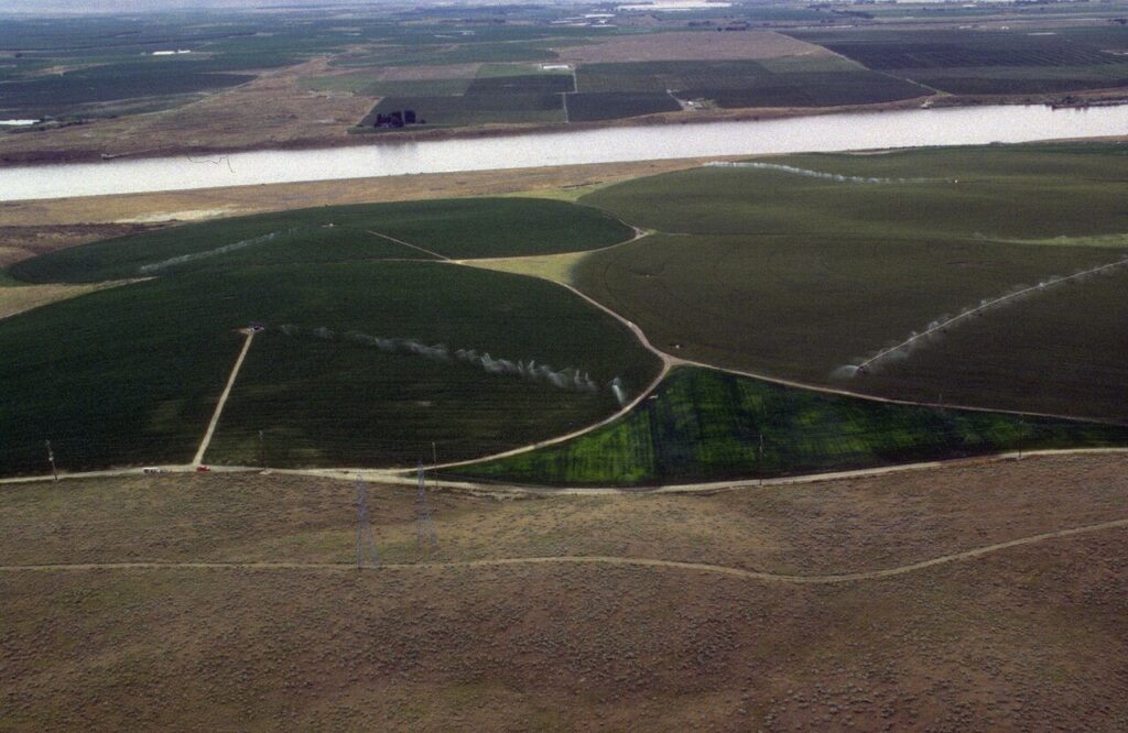 Aerial view of center-pivot sprinklers irrigating circular fields beside a river in Idaho