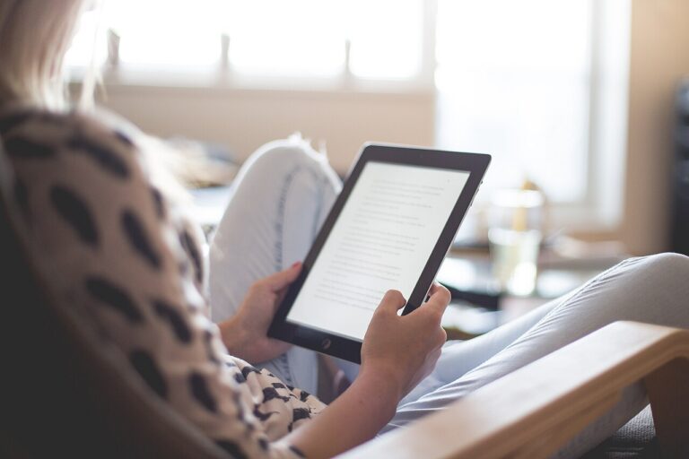 Person seated in a chair holding a tablet with text on its screen